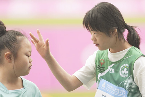 ◎ 十二月十一日,在女子八至十一歲組五十米預賽賽前,澳門一團隊田徑選手陳曉琳(右)和新疆生產建設兵團隊選手盛馨玥交流。(新華社記者 楊晨光攝 )