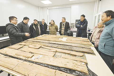 ◎ 中國社會科學院科技考古與文化遺產保護重點實驗室副研究員劉勇(左一)在實驗室考古方艙內向專家們介紹墓葬M20出土的木棺彩繪情況(二月一日攝)。(新華社記者李賀 攝)